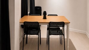 Una habitación con una mesa de madera, dos sillas negras, una lámpara negra y una ventana con cortinas negras.