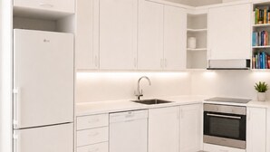 Una cocina moderna con armarios blancos, lavavajillas integrado, horno de acero inoxidable y una estantería con libros.