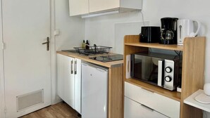 Pieni, käytännöllinen keittiönurkkaus, jossa on valkoinen jääkaappi, mikroaaltouuni, kahvinkeitin ja tiskiallas, jonka yläpuolella on astiateline.
