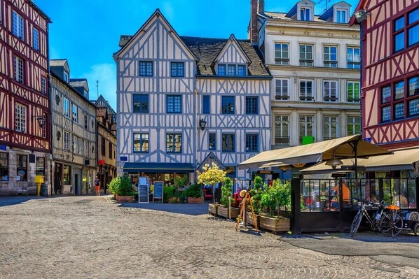 Une rue pavée bordée de bâtiments traditionnels à colombages, un café avec des tables en terrasse et un vélo garé près de l’entrée.