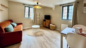 Een woonkamer met een rode bank, een ronde salontafel, een tv-meubel en een eettafel met stoelen.