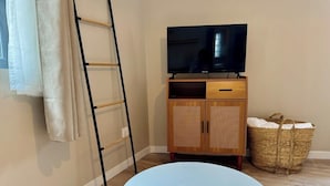 Een kamer met een ronde blauwe tafel, een houten kast met een televisie, een rieten mand en een ladder tegen de muur.