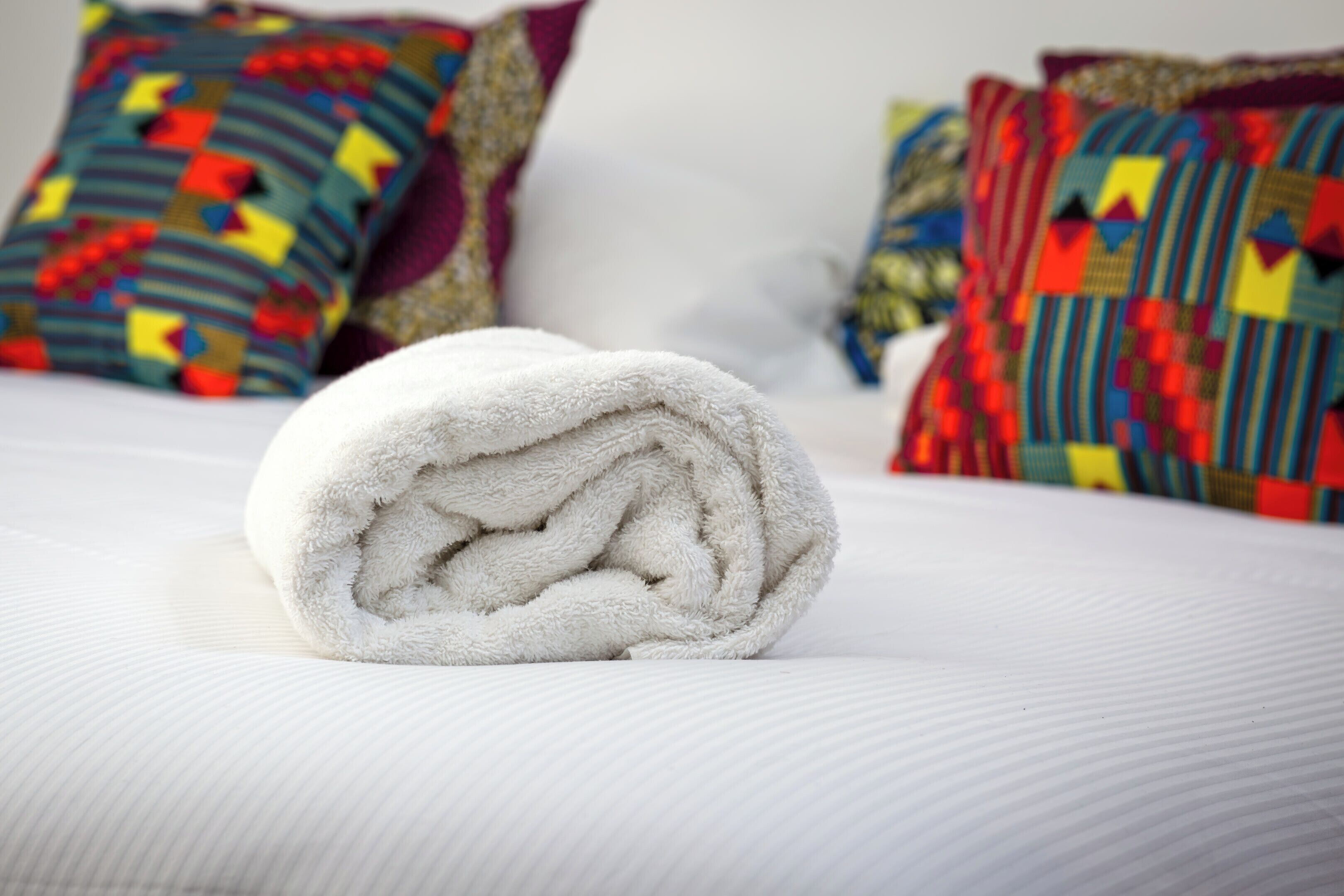 Een keurig opgerolde witte handdoek op een bed met een wit geweven beddegoed.