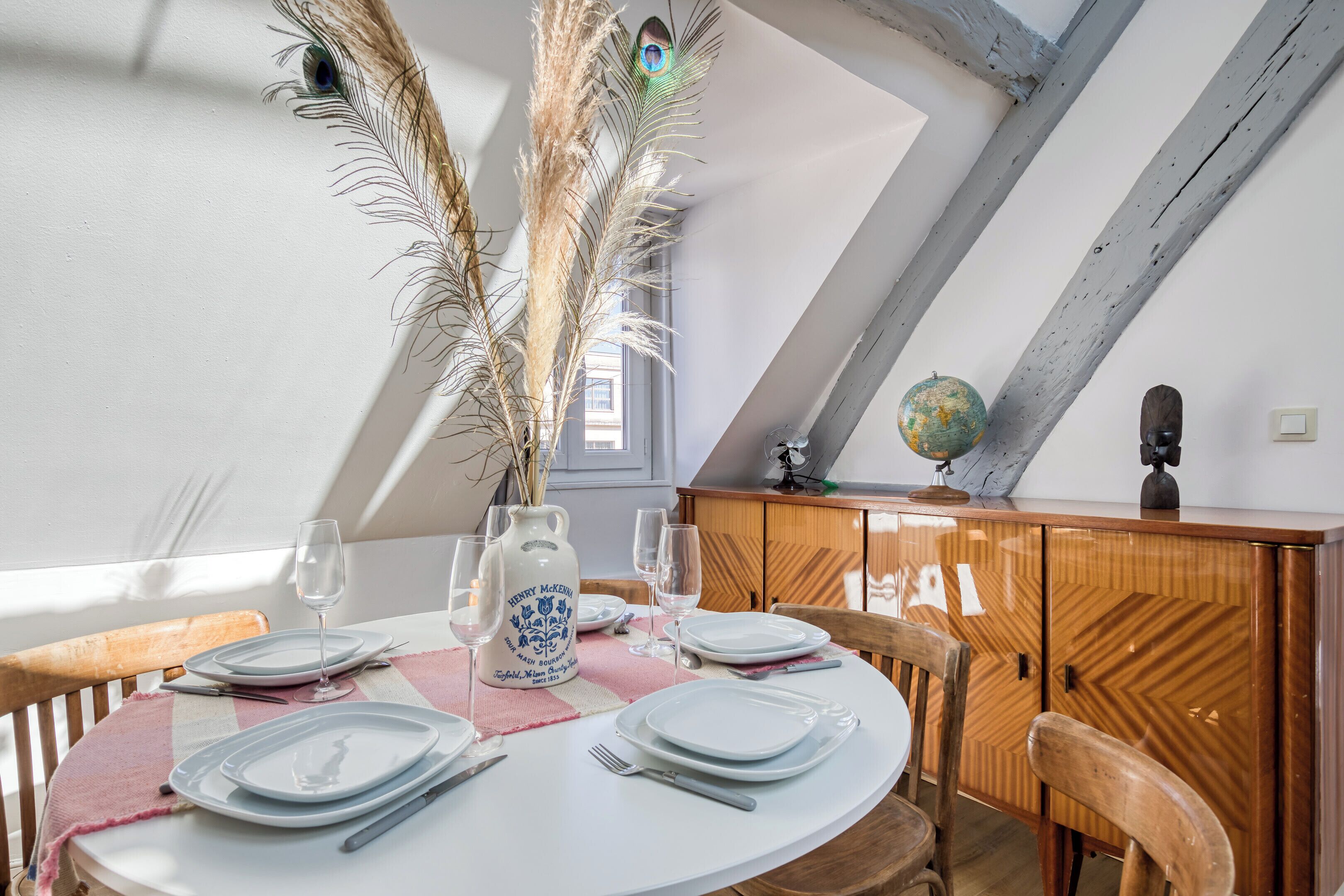 Een eetgedeelte met een ronde tafel gedekt voor vier personen, een houten kast en een wereldbol erbovenop.