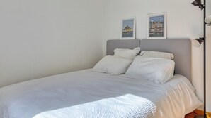 Ein ordentlich bezogenes Bett mit weißer Bettwäsche, einem grauen Kopfteil und zwei gerahmten Bildern an der Wand.