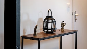 Un couloir orné d’une œuvre d’art fixée au mur, représentant un gros plan de lèvres, d’une petite table sur laquelle se trouvent un panier noir et une sculpture, ainsi que d’une porte dotée d’une poignée.
