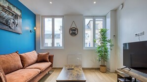 Ett vardagsrum med en soffa, ett soffbord, en tv och ett stort fönster med utsikt över byggnader.