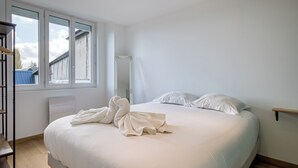 Ett sovrum med en stor säng, en träbänk och ett fönster med utsikt över en byggnad utanför.