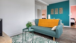 Un salon moderne avec un canapé de couleur turquoise, une petite table d’appoint ornée d’une plante et un tapis à motifs.