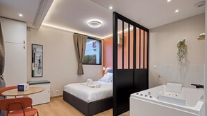 Een moderne hotelkamer met een bed, een klein tafeltje met een stoel, een bureau, een bureaustoel, een badkuip en een raam met gordijnen.