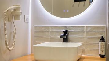 A bathroom with a white sink, a round mirror with a light, and a hairdryer mounted on the wall.