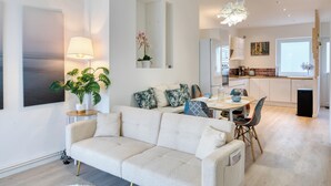 Un salon moderne comprenant un canapé, une table à manger avec des chaises, un coin cuisine avec un réfrigérateur et un luminaire suspendu.