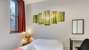 Hotelkamer met een bed, een bureau, een stoel, een raam met rode gordijnen en een muur met bosdecoratie.