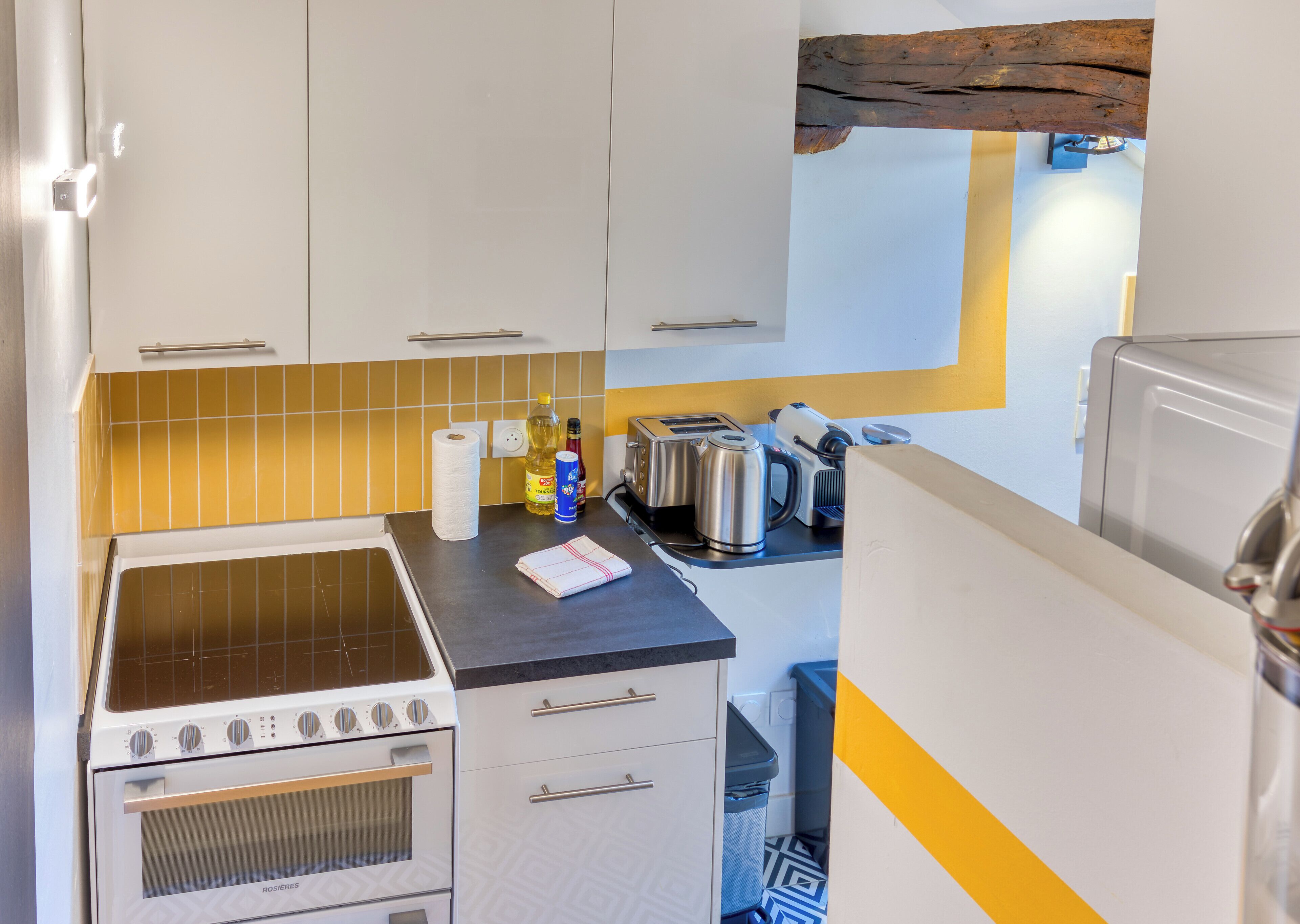 A compact kitchen with a stove, oven, and a toaster. There are cabinets, a countertop, and a trash bin.