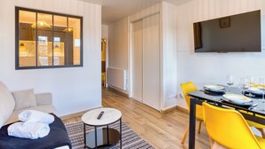 Una sala de estar moderna con un sofá, una mesa redonda de centro y un comedor con sillas amarillas y una mesa dispuesta para dos personas.