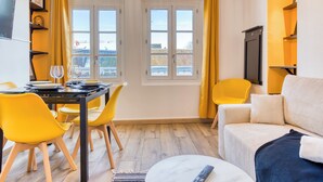 Una sala de estar moderna con comedor, sillas amarillas, un sofá y un televisor en la pared.