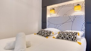 Una habitación de hotel moderna con una cama grande, cabecera estampada y dos lámparas fijadas a la pared.
