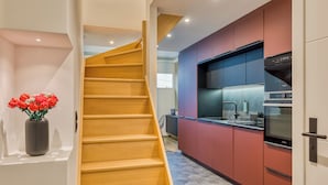 Une cuisine moderne avec des meubles rouges, un four encastré et un escalier en bois menant à un autre niveau.