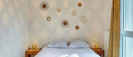 A neatly made bed with white linens and two rolled towels, a wooden nightstand with a lamp, and decorative wall art.