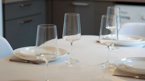 A dining table set with clear wine glasses and white plates, in a modern kitchen with grey cabinets. - Le Nicole, un appartement en duplex avec balcon et place de parking. (Rouen)