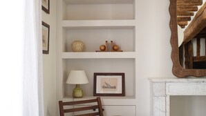 Une pièce comprenant une chaise en bois, une étagère blanche ornée d’objets décoratifs et un miroir.