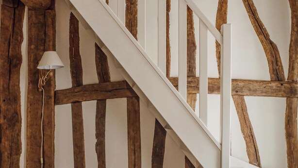 Un escalier avec des poutres en bois apparentes et une rampe blanche.