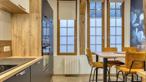 A modern kitchen with wooden cabinets, a built-in oven, and a dining area with yellow chairs and a table. - L'escale du Gros-Horloge, une parenthèse prestigieuse au coeur de Rouen (Rouen)