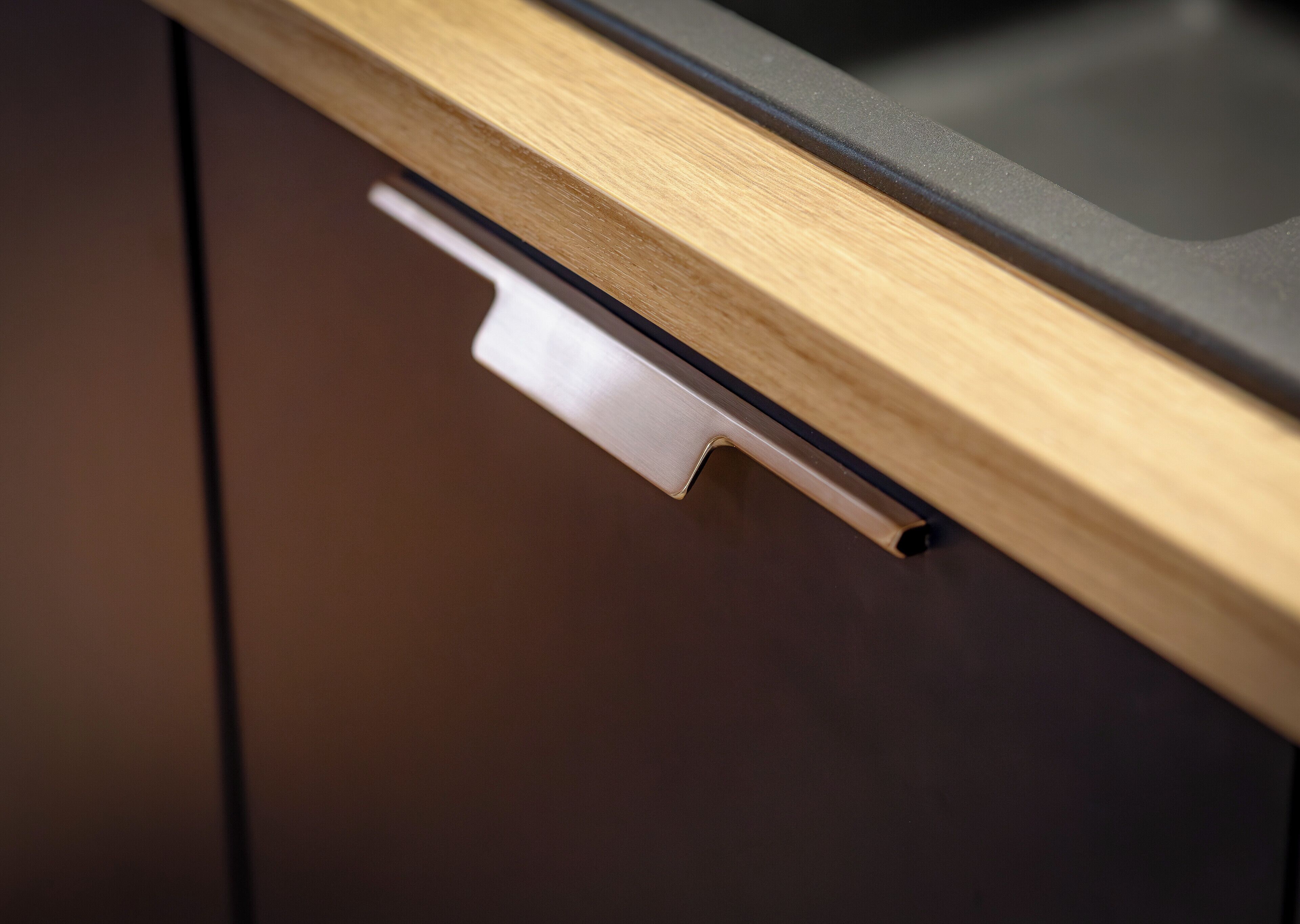 A close-up of a kitchen drawer with a wooden handle and a metallic pull.