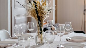 A dining table set with white plates, clear wine glasses, and a vase with dried flowers. - Agapanthes, jolie maison de ville à Rouen avec extérieur, terrasse (Rouen)