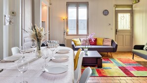 A dining area with a table set for four, a sofa, and a colorful rug. - Agapanthes, jolie maison de ville à Rouen avec extérieur, terrasse (Rouen)