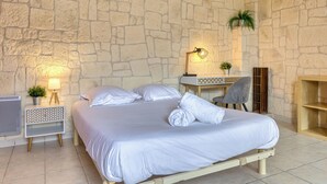 A bedroom with a stone wall, a bed with white linens, a desk with a lamp, and a chair. - Agapanthes, jolie maison de ville à Rouen avec extérieur, terrasse (Rouen)
