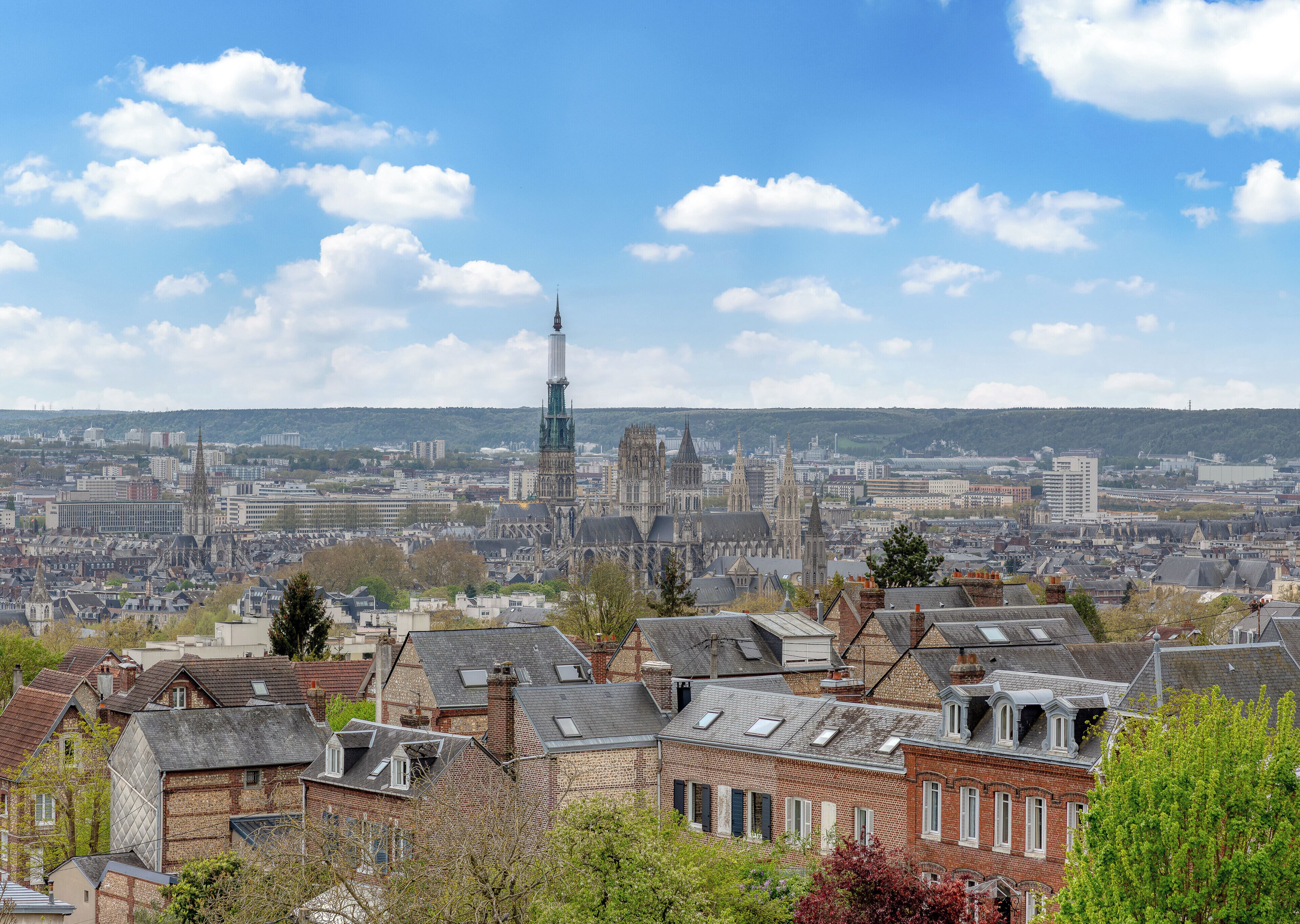 A cityscape with historic architecture, including a prominent cathedral with a tall spire, surrounded by residential buildings and a clear blue sky.