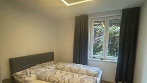 Une chambre à coucher moderne avec un lit, une table de chevet, une fenêtre avec des rideaux et un luminaire au plafond.