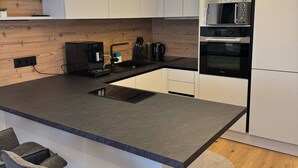 Une cuisine moderne avec des meubles blancs, un îlot central doté de tabourets, un four encastré et un four à micro-ondes.