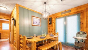 Interior de una cabaña de madera con una mesa de comedor, bancos, una trona y un cuadro en la pared.