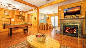 Un interior de madera con mesa de billar, chimenea y televisor montado en la pared.