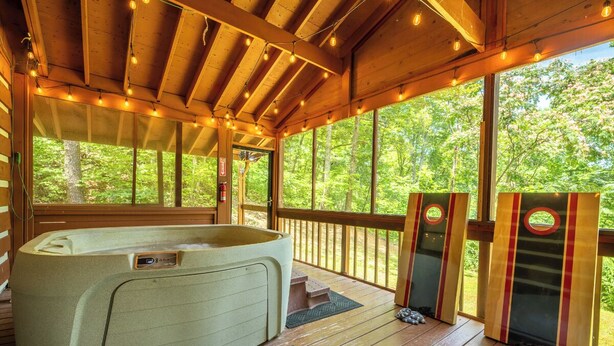 Terraza de madera con jacuzzi, ventanas amplias y vista a árboles.