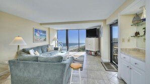 A spacious living room with a large sofa, a small table, and a view of the ocean through large windows.