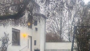 Un edificio blanco con una escalera que lleva a una puerta, rodeado de césped y un sendero pavimentado.