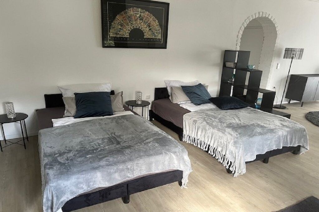 A bedroom with two beds, a small table, a bookshelf, and a decorative wall piece.