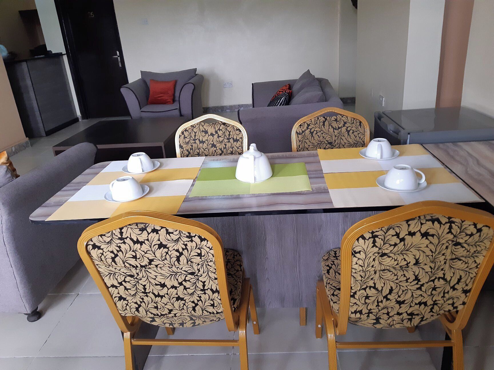 Un coin repas avec une table rectangulaire, quatre chaises à l’assise tapissée d’un motif décoratif et un canapé en arrière-plan.