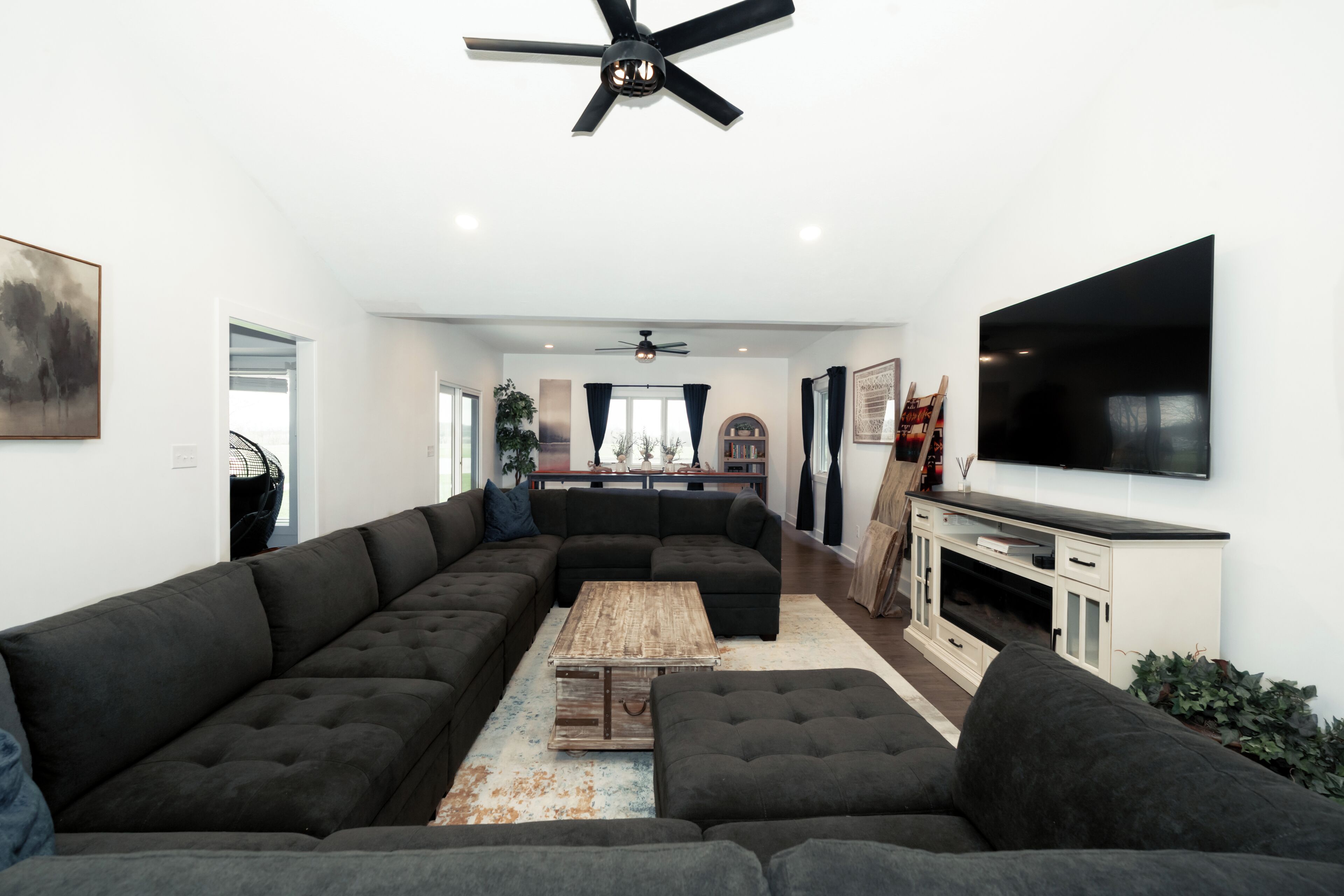 A modern living room with a sectional sofa, a coffee table, and a flat-screen TV mounted on the wall.