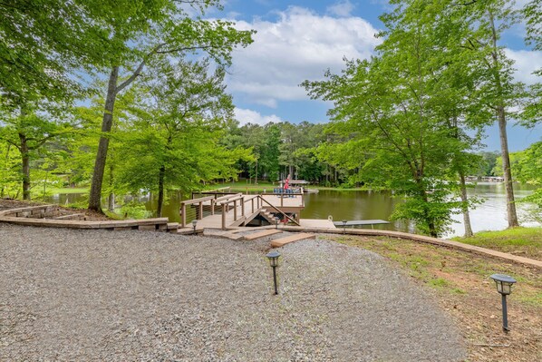 A gravel area with a wooden deck leading to a dock over water, surrounded by trees. - New:Lakefront, Firepit, Deck, Dock, Kayak, Great times on Lake Gaston (Littleton)