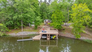 A wooden dock with a small cabin, surrounded by dense green trees and a calm body of water.