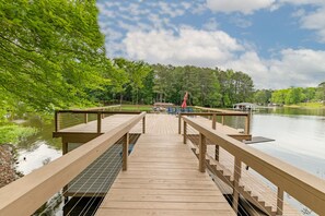 A wooden deck leading to a dock over a calm lake, surrounded by lush greenery and a clear sky. - New:Lakefront, Firepit, Deck, Dock, Kayak, Great times on Lake Gaston (Littleton)