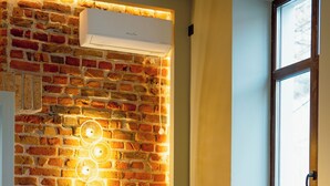 Een kamer met een bakstenen muur, een groene bank, een rond poef en een raam.