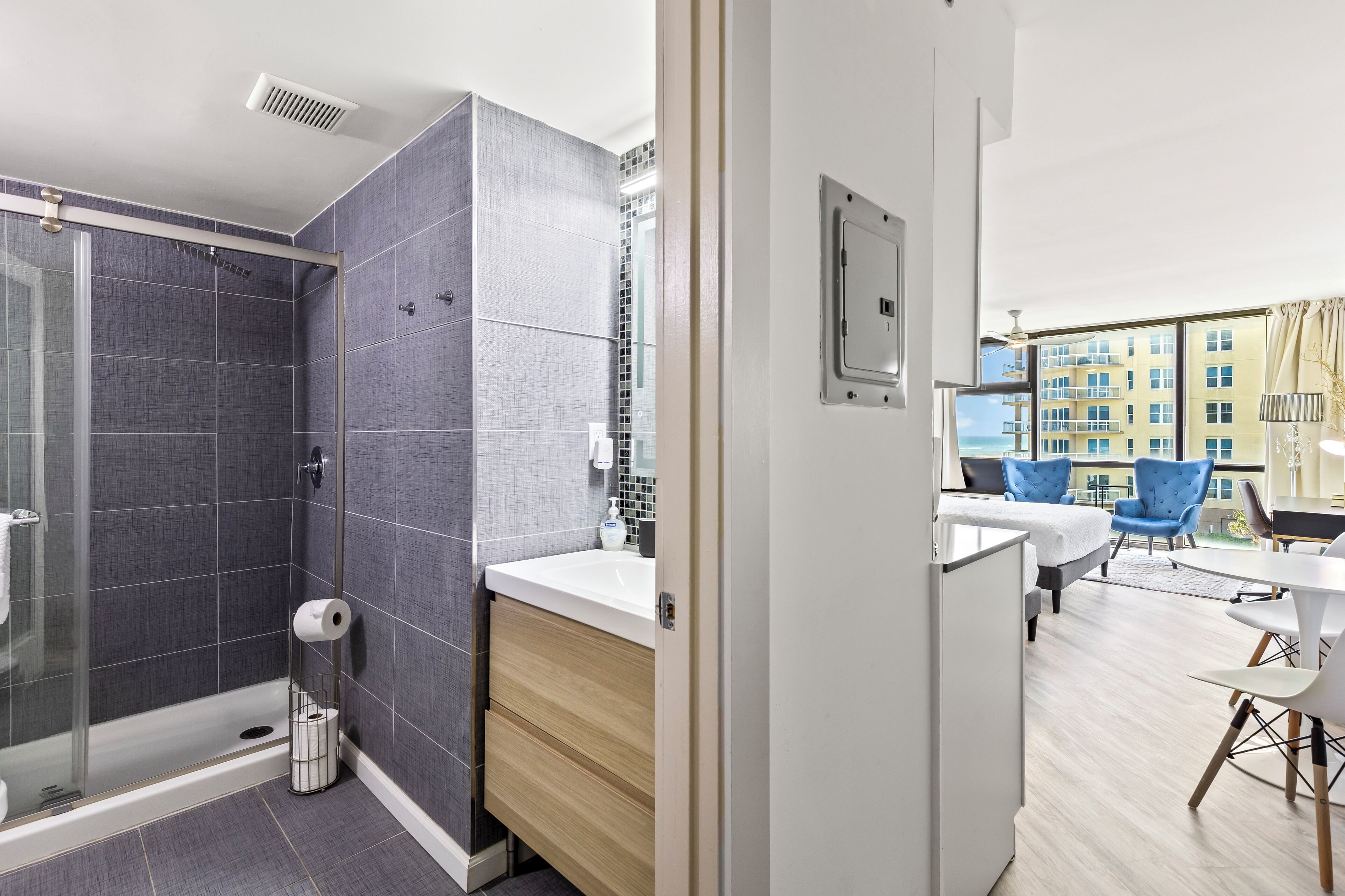 A modern bathroom with a shower, toilet, and sink. There is a balcony with a view of buildings.