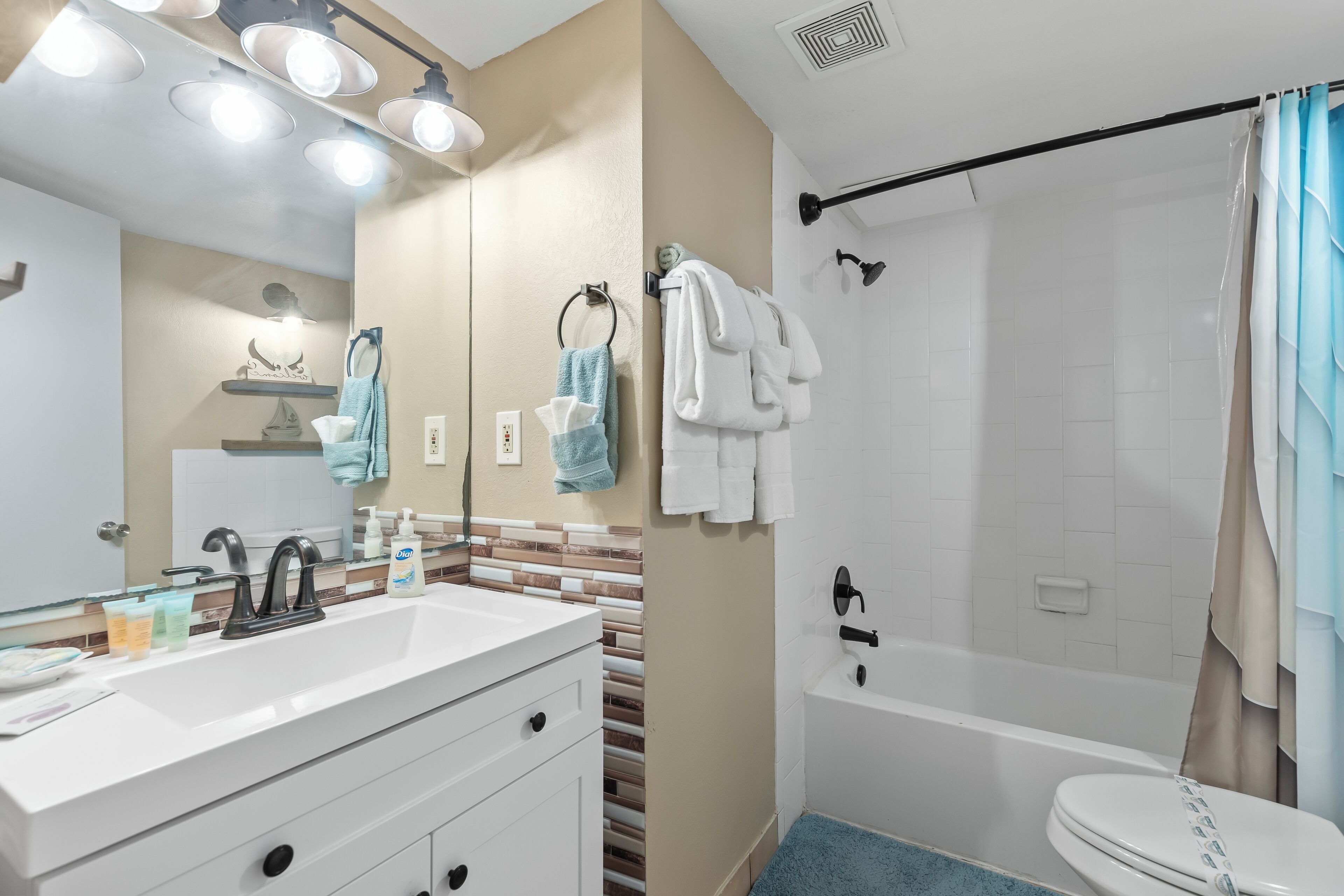 A bathroom with a white sink, mirror, and towel rack. There is a bathtub with a shower curtain and a toilet.
