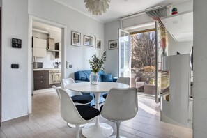 Eine moderne Küche mit weißen Schränken, einem Esstisch mit weißen Stühlen und einem großen Fenster mit Blick auf Bäume.