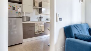 Ett modernt kök med ett kylskåp i rostfritt stål, en mikrovågsugn och en inbyggd ugn. Köket har också en barstol och en diskho.